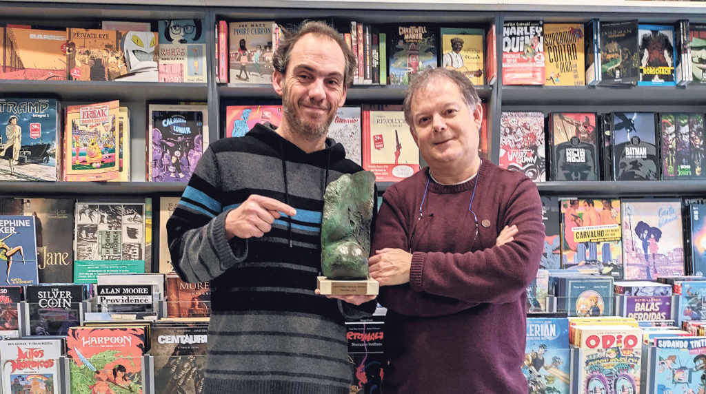 Xaime Lis e Xosé Barreiro, na libraría Komic, co galardón que recibiron esta semana polo compromiso co galego (Nós Diario).
