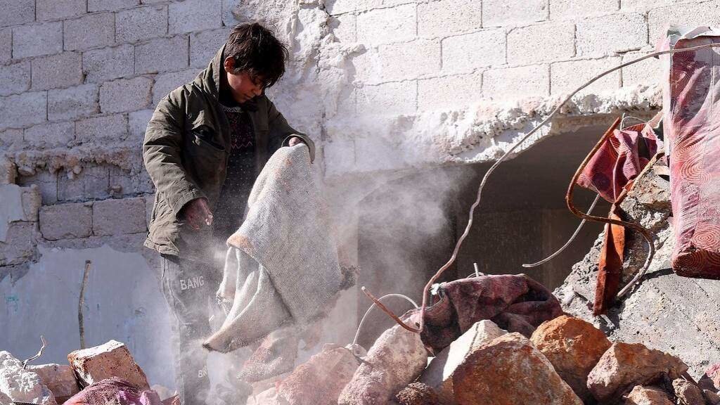 Un mozo rebusca entre os cascallos dun edificio derruído na cidade siria de Aleppo. (Foto: Stringer / Xinhua News)