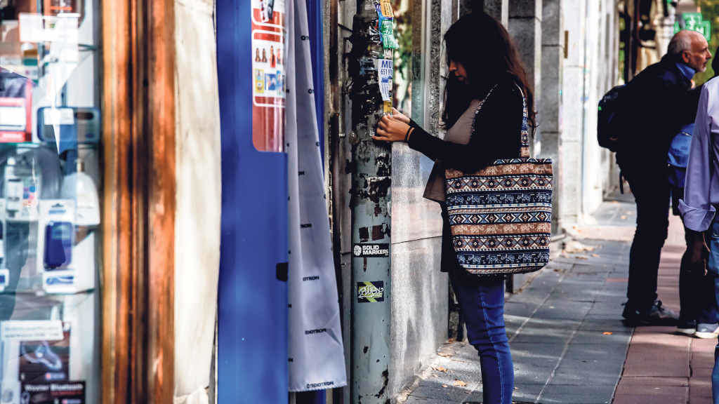 Unha moza pega un papel nun farol onde se comparten anuncios de 'busco emprego' (Foto: Carlos Luján / Europa Press).