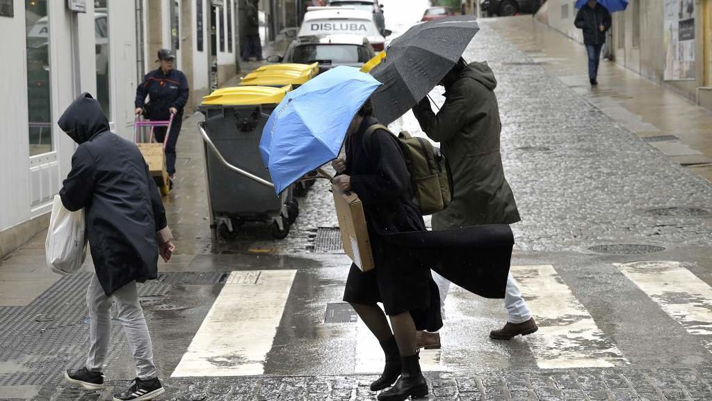 Dúas persoas tratan de refuxiarse da choiva cos seus paraugas na Coruña. (Foto: M. Dylan / Europa Press)