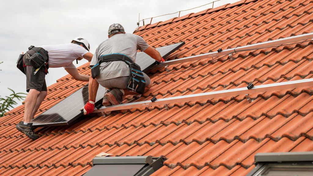 Dous traballadores instalan un panel fotovoltaico no tellado dunha casa particular. (Foto:  Dziurek).