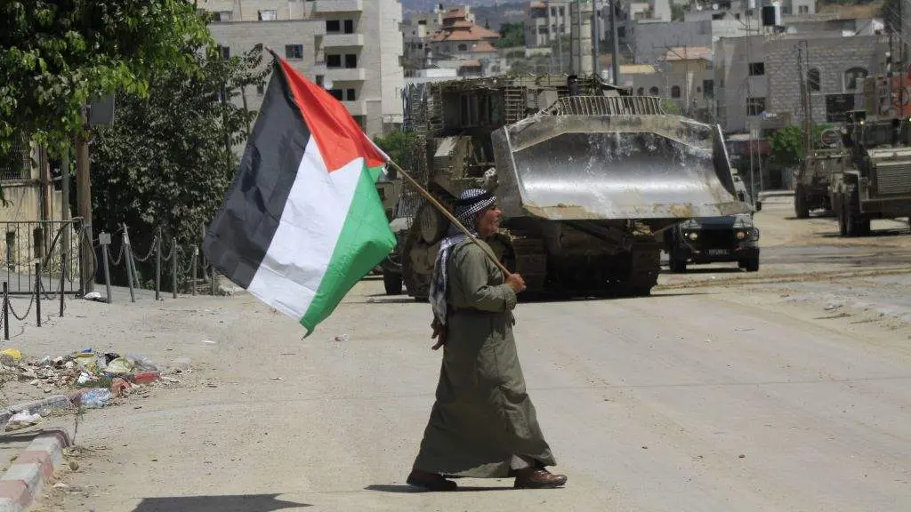 Un home porta unha bandeira de Palestina ante os veh&iacute;culos militares de Israel que patrullan as r&uacute;as de Tulkarm, en Cisxordania. (Foto: Mohammed Nasser / APA Images via Z / DPA)
