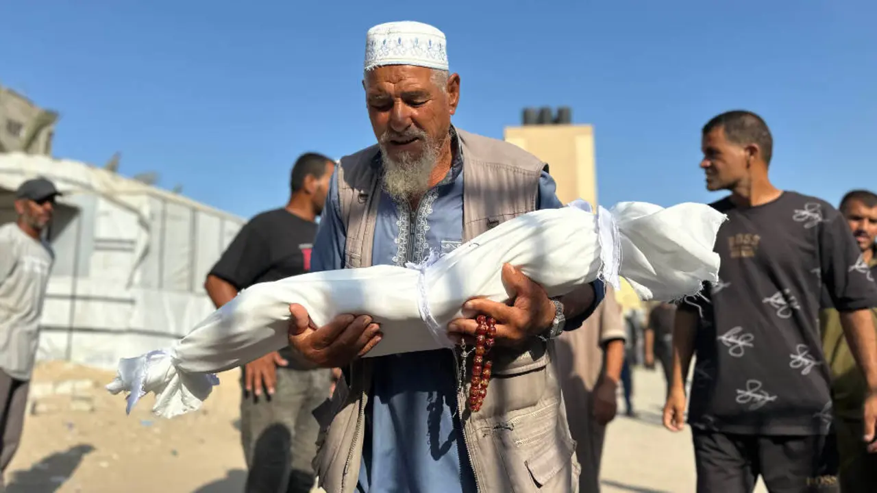 Un home portando o 20 de agosto de 2025 o corpo dunha crianza asasinada polos bombardeos israel&iacute;s en Khan Younis, no sur da Faixa de Gaza. (Foto: Mohammed Salama / APA Images)