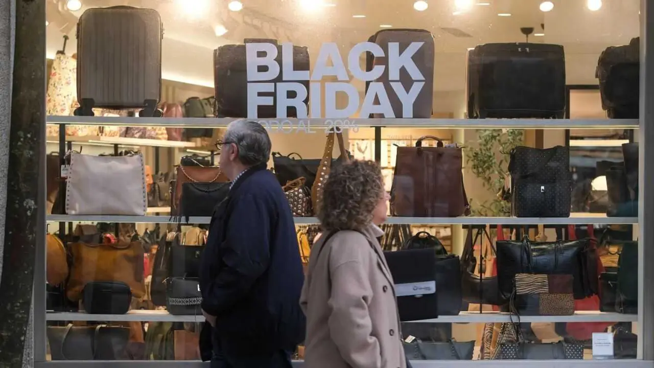 D&uacute;as persoas pasan por diante dun escaparate onde se anuncia o Black Friday. (Foto: Arxina)