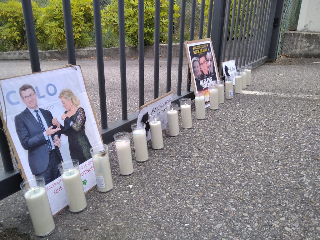 Velas e pancartas con fotos de Feixoo e a directora de DomusVi na porta da residencia de maiores de Aldán, en Cangas.